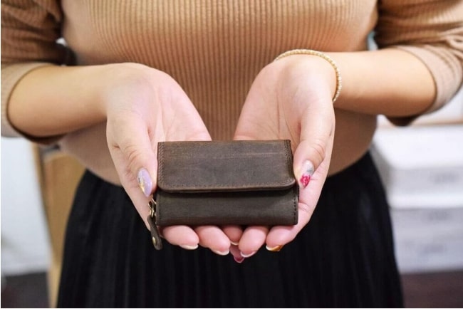 カードサイズに近い大きさに作られた三つ折りミニ財布を手のひらに乗せる女性