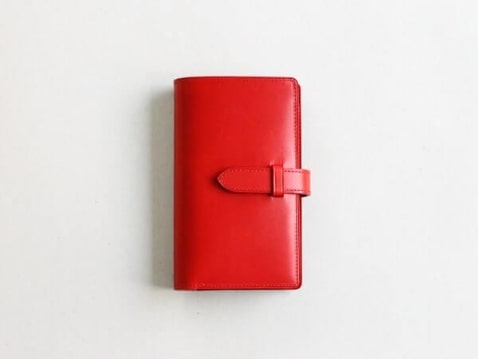 手帳のようなストラップで留めるデザインの赤い二つ折り財布