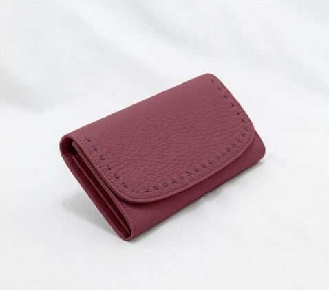 手縫いで仕上げる革紐ステッチが特徴的な赤紫色のかぶせ式長財布